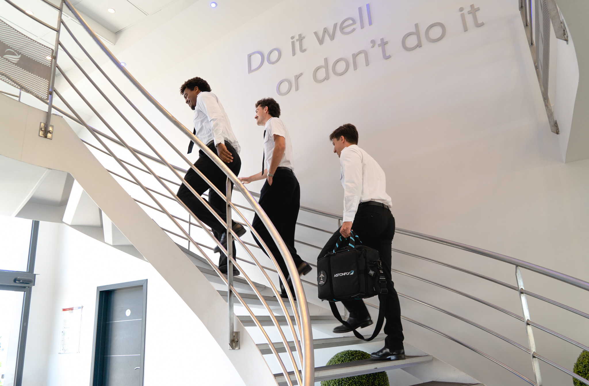 Élèves pilotes Astonfly montant l'escalier sous la devise « Do it well or don't do it »